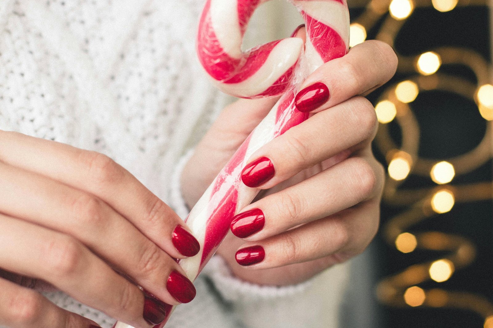 Close-up of hands with red nails holding a candy cane, perfect for Christmas-themed visuals.