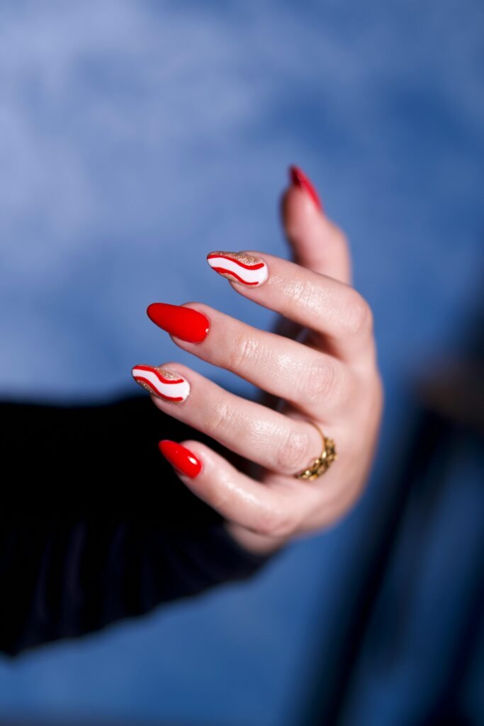 Close-up of a hand showcasing red nails with artistic wave design.