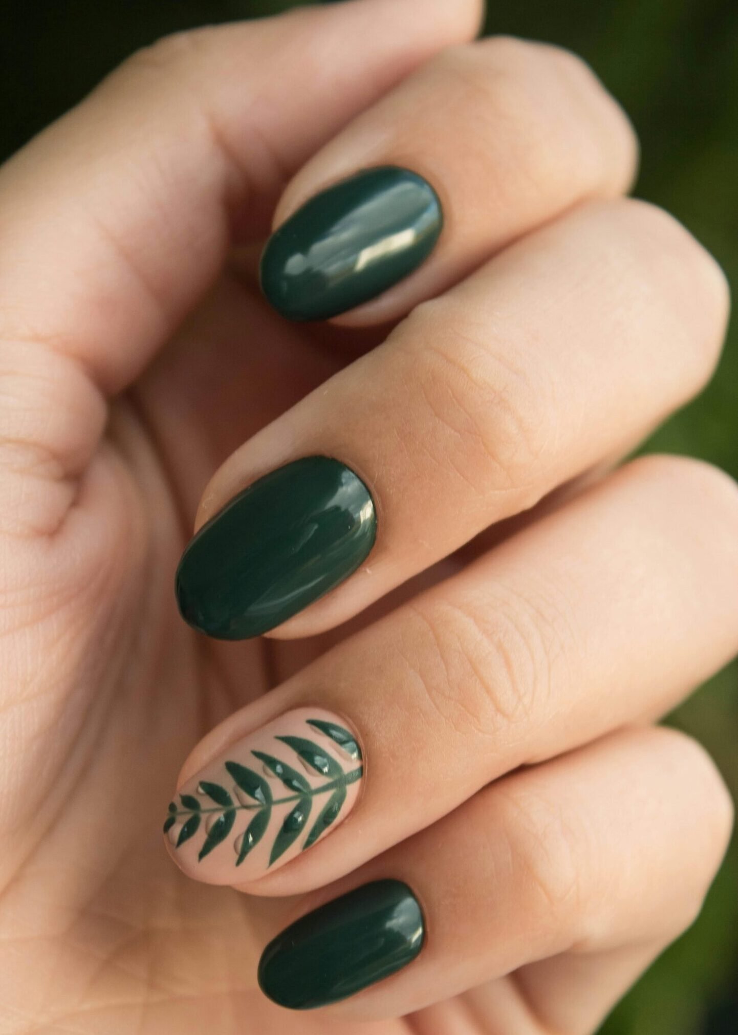 Close-up of a stylish green manicure with a leaf design, showcasing glossy fingernails and natural skin tone.